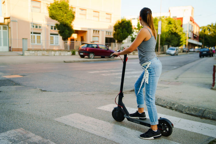Young woman standing on electric push scooter on street