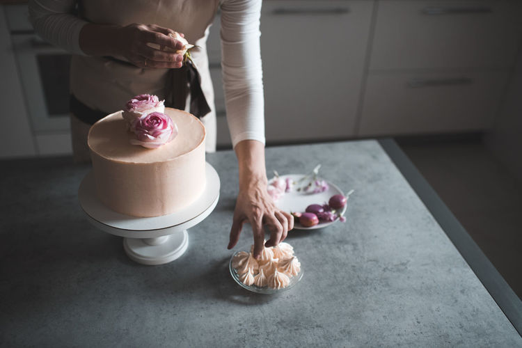 Woman making cake decorating with flower roses staying on kitchen table close up at home. 