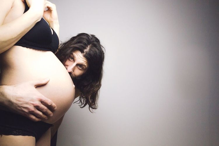 Portrait of man standing by pregnant woman against wall