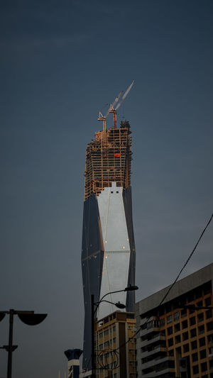 Low angle view of crane by building against sky