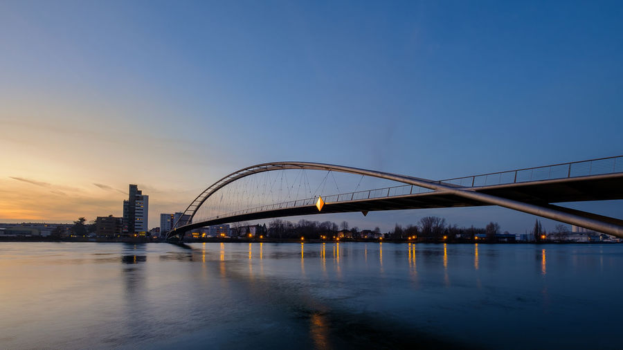 Bridge over river in city against sky during sunset