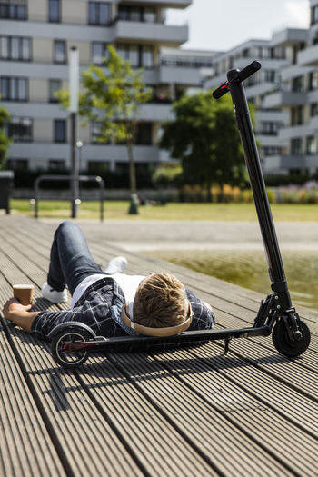 Young man with e-scooter lying on boardwalk
