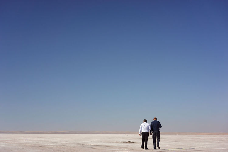 Men walking on salt flat against clear sky