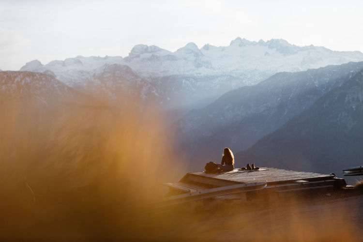 Side view of unrecognizable female tourist sitting at viewpoint in mountains and observing amazing scenery in morning