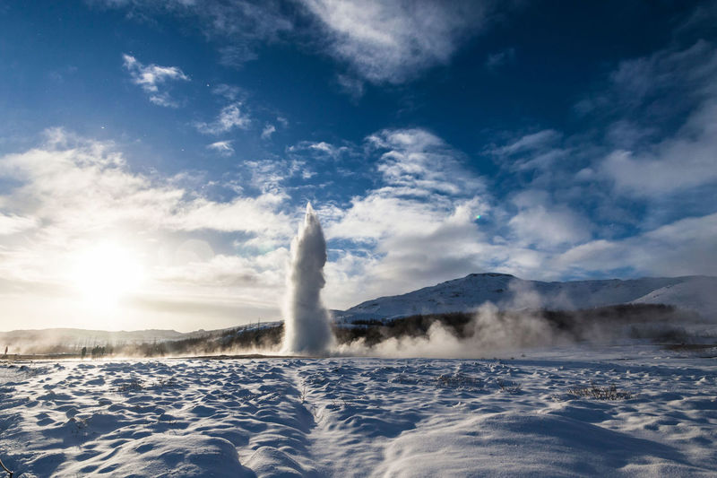 Geyser by snow field against sky
