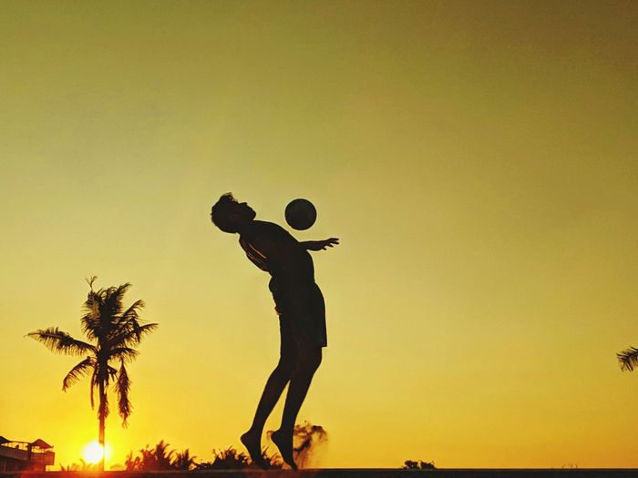 Side view of silhouette man playing beach volleyball against sky during sunset