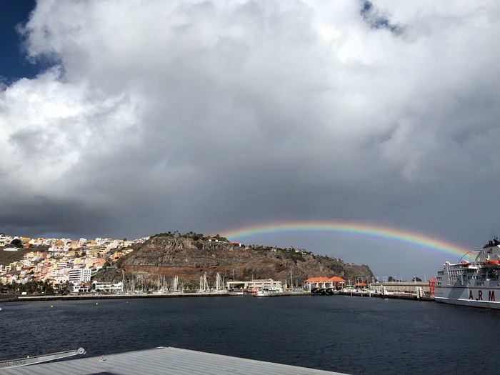 Scenic view of rainbow over city by sea against sky