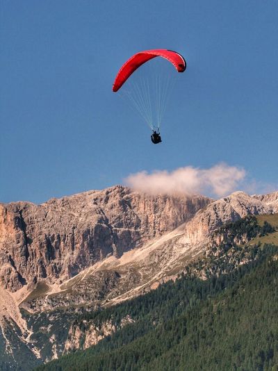 Person paragliding above forest trees and mountains against sky
