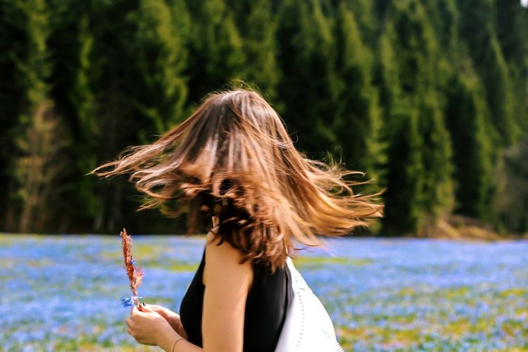 Woman tossing hair while standing by lake against tree