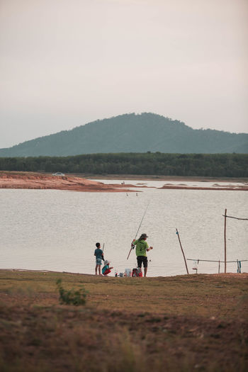 People fishing in lake against sky