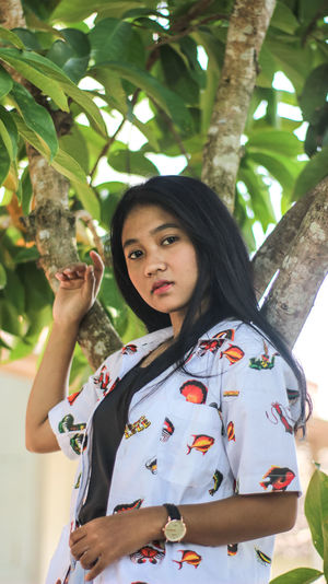Portrait of young woman standing against tree