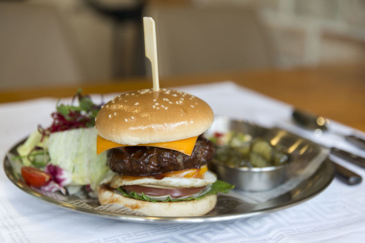 Close-up of hamburger with salad and pickle served in plate on table