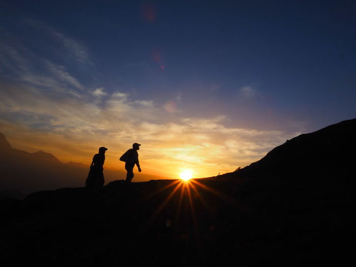 Silhouette men on mountain against sky during sunset