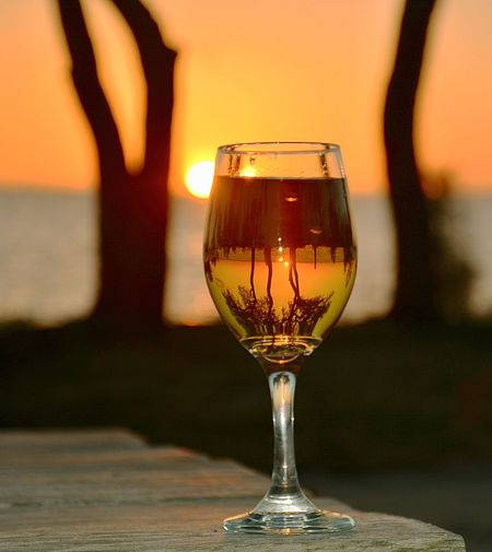 Close-up of wineglass on table against sea during sunset
