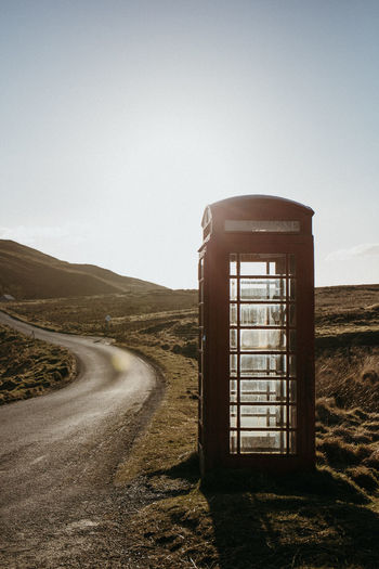 Telephone booth by road against clear sky