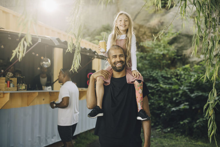 Smiling father carrying daughter on shoulders by food truck