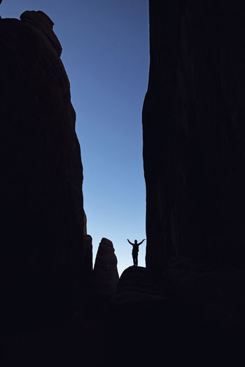 Hiker stands silhouetted in deep canyon with blue sky, moab utah