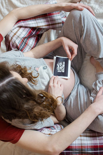 Midsection of pregnant woman holding instant print transfer while sitting with man