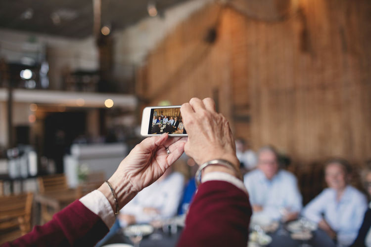 Cropped image of senior woman photographing friends with smart phone at restaurant