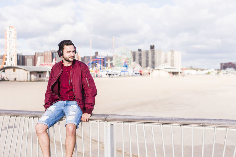 Usa, new york city, man sitting on railing on coney island wearing headphones