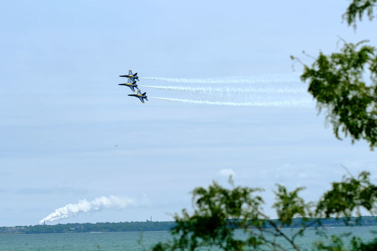 Low angle view of airshow flying over sea against sky