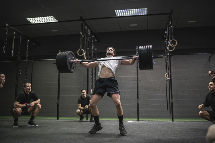 People cheering man lifting barbell while standing in gym