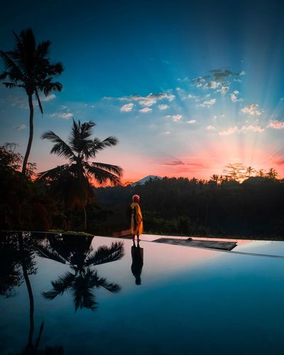 Woman standing by poolside against sky during sunset