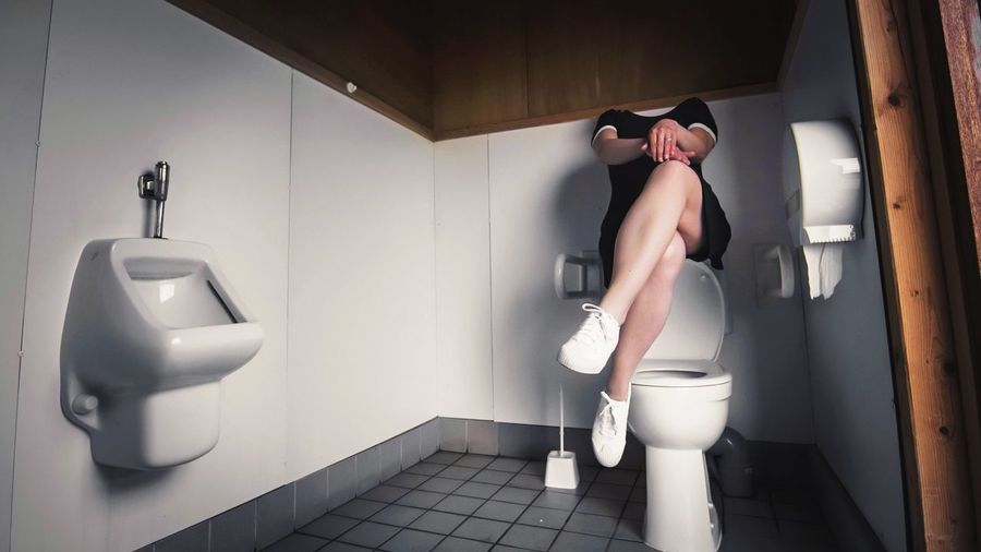 Woman sitting over commode at public toilet