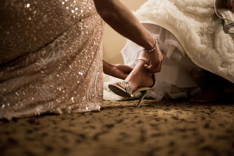 Low section of woman assisting bride in wearing sandals