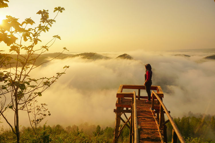 Woman standing at observation point against cloudy sky during sunset