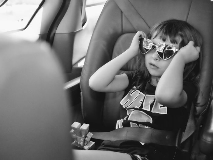 Cute girl wearing heart shape sunglasses sitting in car