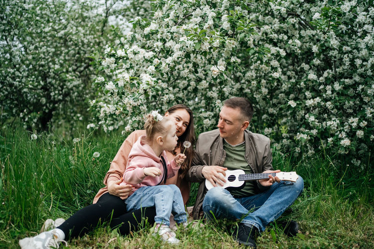 Family mom mom baby daughter in the garden blooming apple trees, father playing the ukulele