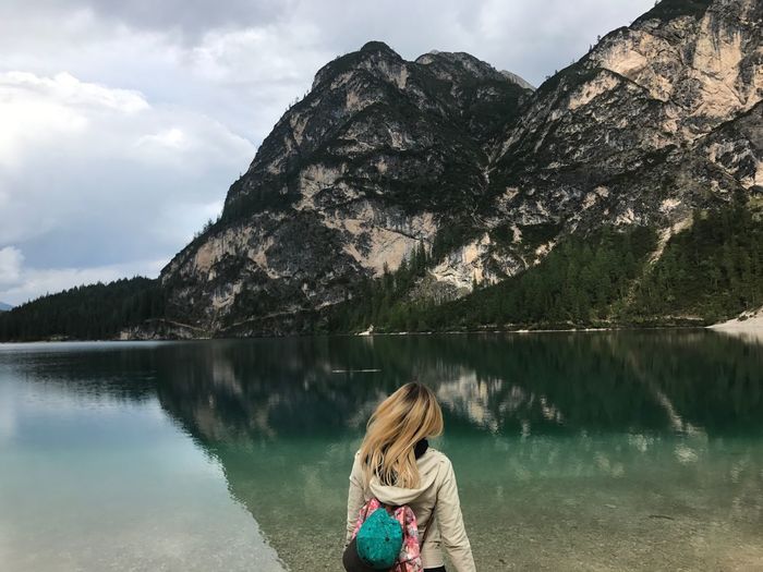 Rear view of young woman by lake against mountains
