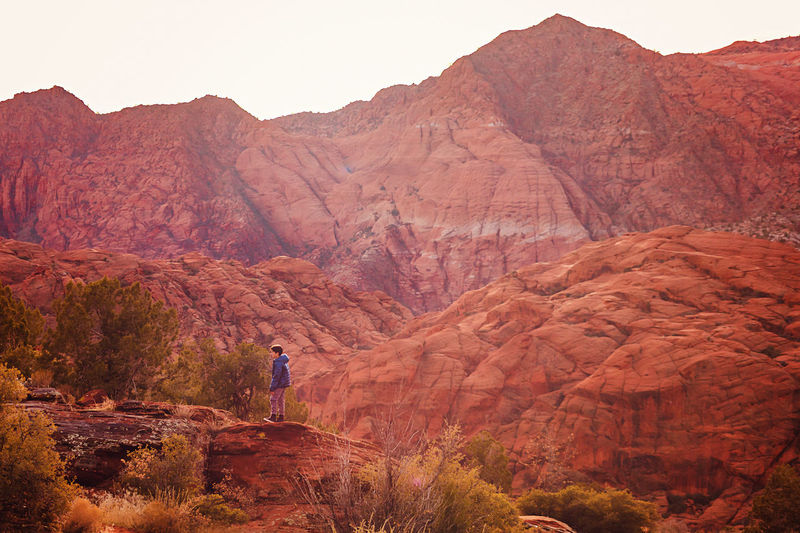 Boy hiking on trail by the red sandstone cliffs and mountains in utah