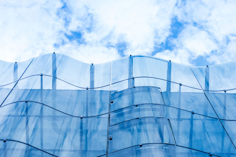 Detail of the wavy glass curtain wall facade of a nice modern building, sky and clouds reflecting