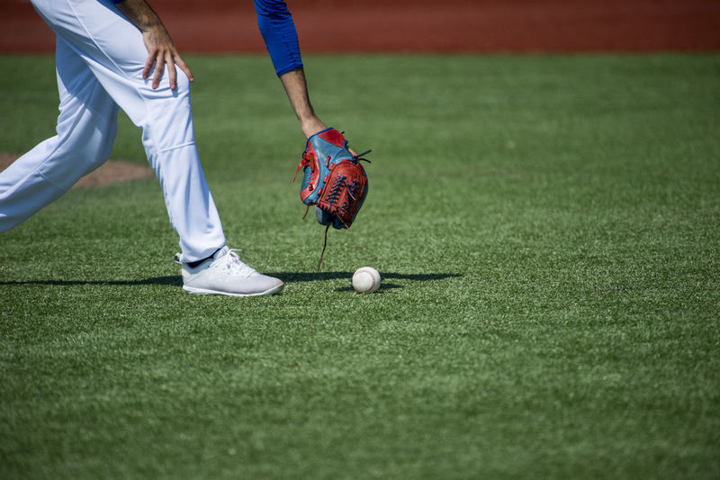 Low section of player picking baseball on grass