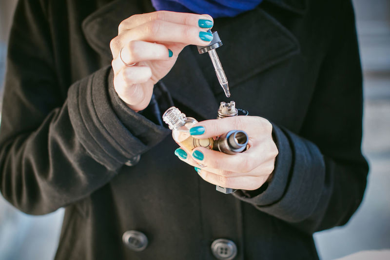 Midsection of woman holding electronic cigarette and dropper