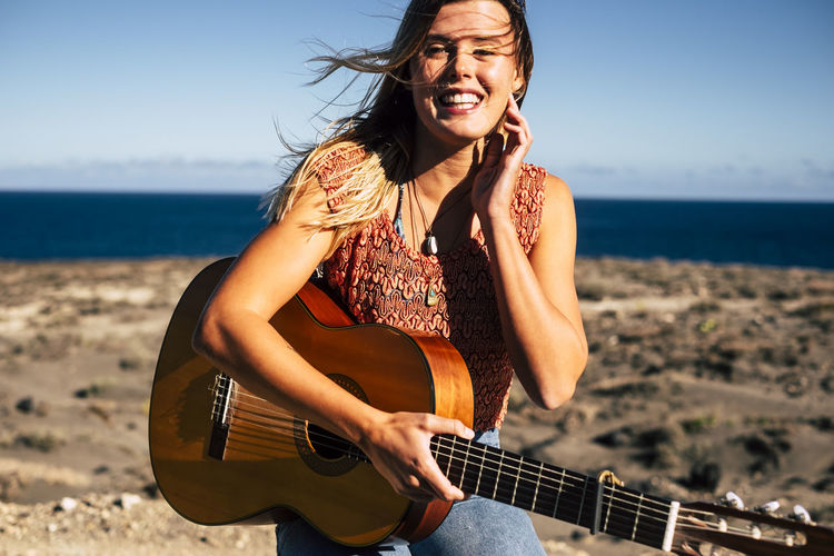 Portrait of young woman with guitar at beach