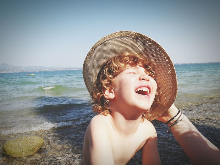Cheerful boy in hat at beach against clear sky