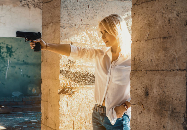 Woman holding gun while standing amidst columns