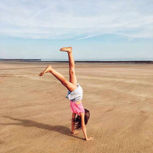 Full length of woman doing handstand at beach against sky