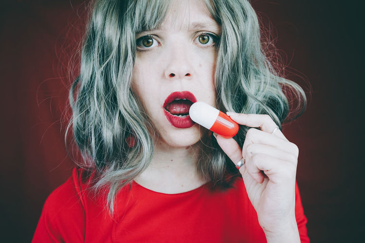 Woman eating capsule against red background