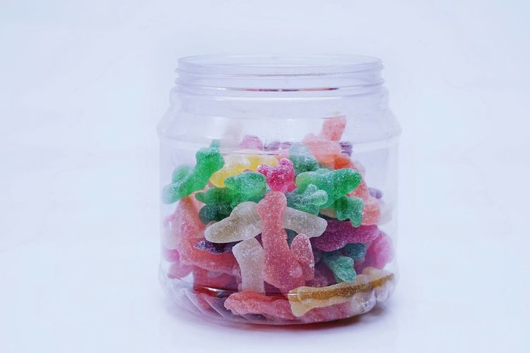 Close-up of multi colored candies in jar against white background