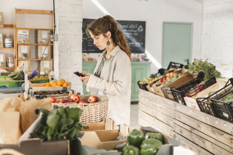 Customer using smart phone standing in vegetable store