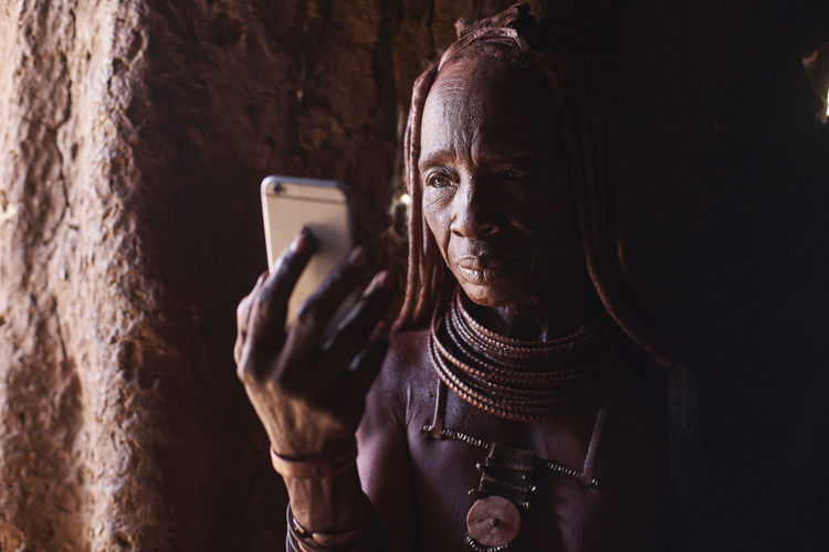 Old himba woman checking her smartphone, oncocua, angola