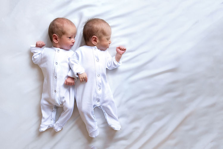 Newborn twins on the bed, in the arms of their parents, on a white background. emotions of kids.