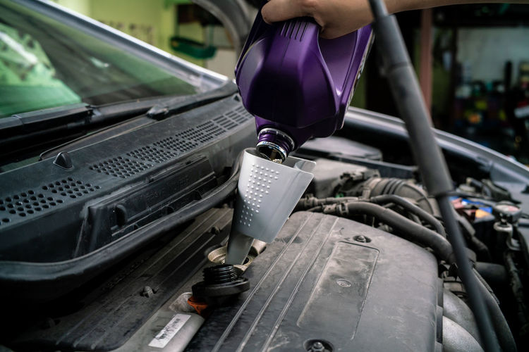 Cropped hand of woman pouring motor oil in garage