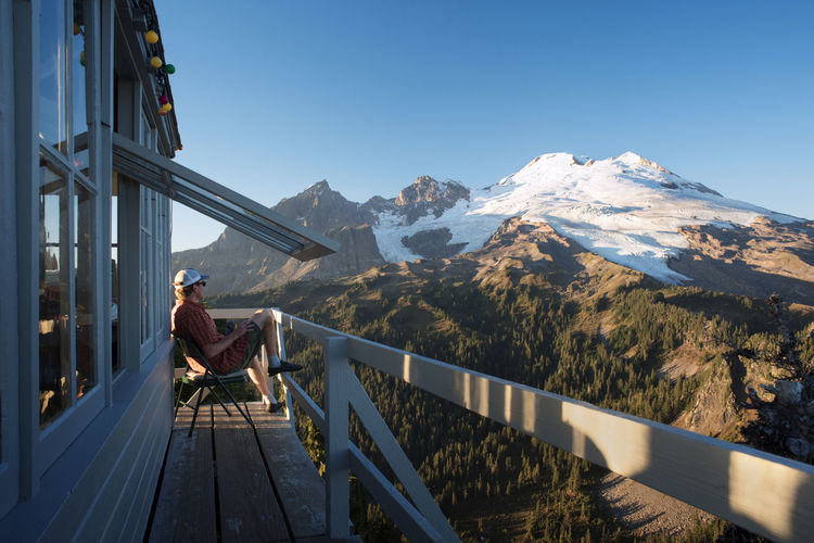 Side view of man sitting on balcony of cottage against mountains