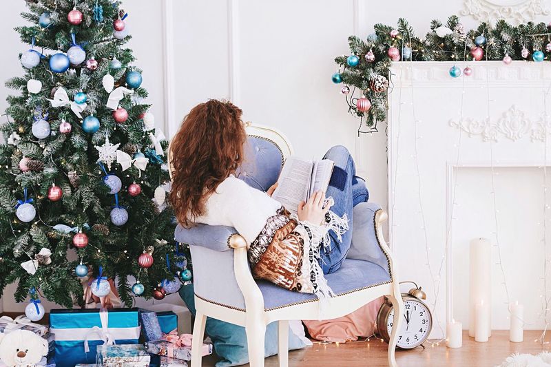 Woman reading book while relaxing on chair by christmas tree at home