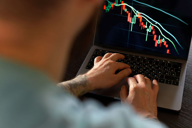 Male hands monitoring stock market numbers and graph on laptop. investment analysis, trading concept